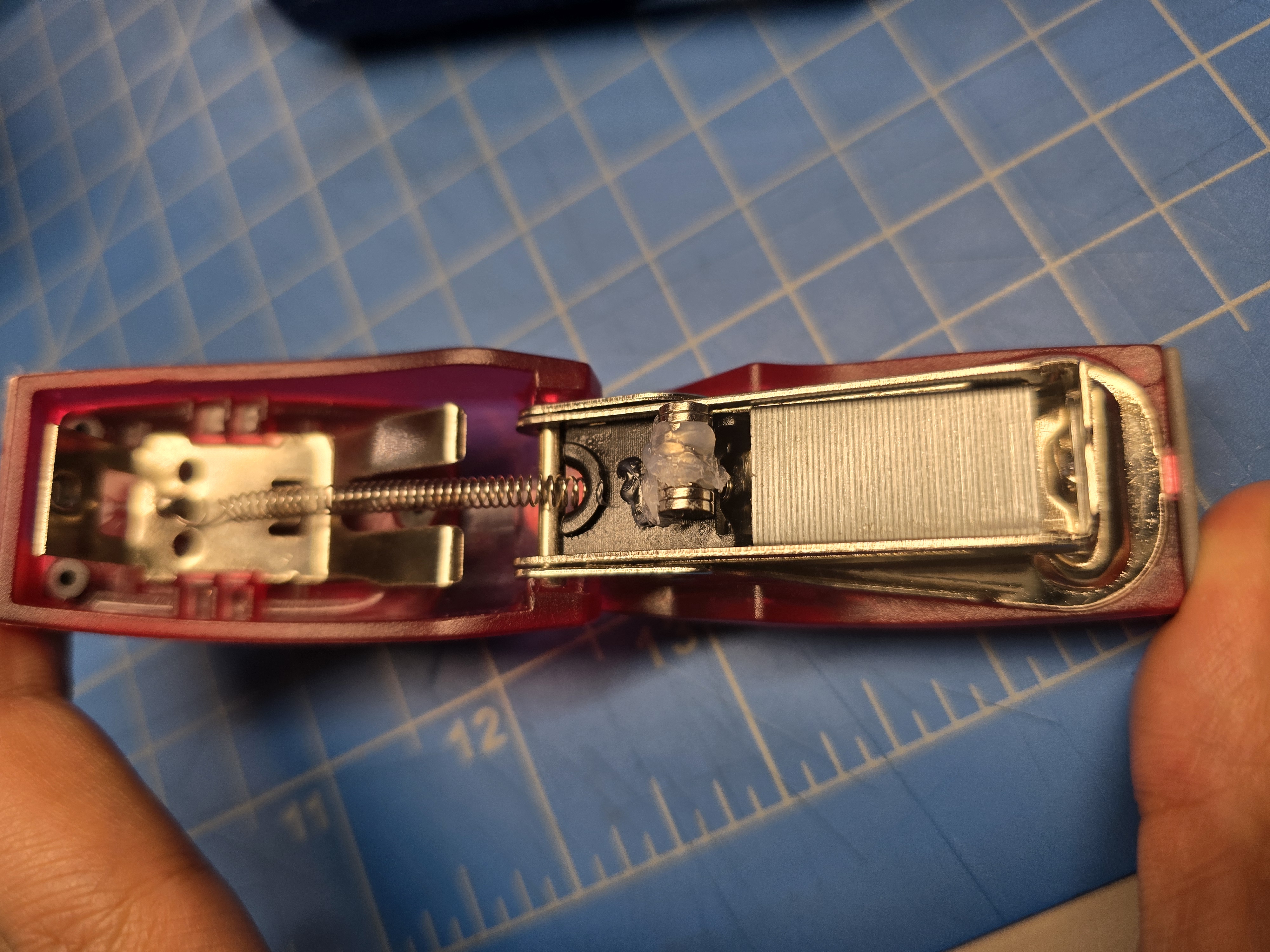 Hot‑gluing magnets to the black bar attached to the spring so the magnets travel with the mechanism without interfering with the staples